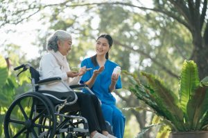 Older woman in wheelchair sitting outside with hospice nurse, taking medication and enjoying outdoors