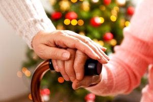 Young person placing comforting hand on older person's hand, which is resting on a cane at Christmas