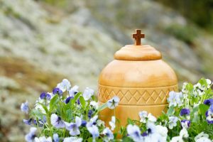 Wooden urn with cross on top, surrounded by purple flowers