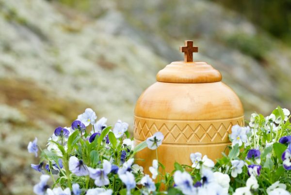 Wooden urn with cross on top, surrounded by purple flowers