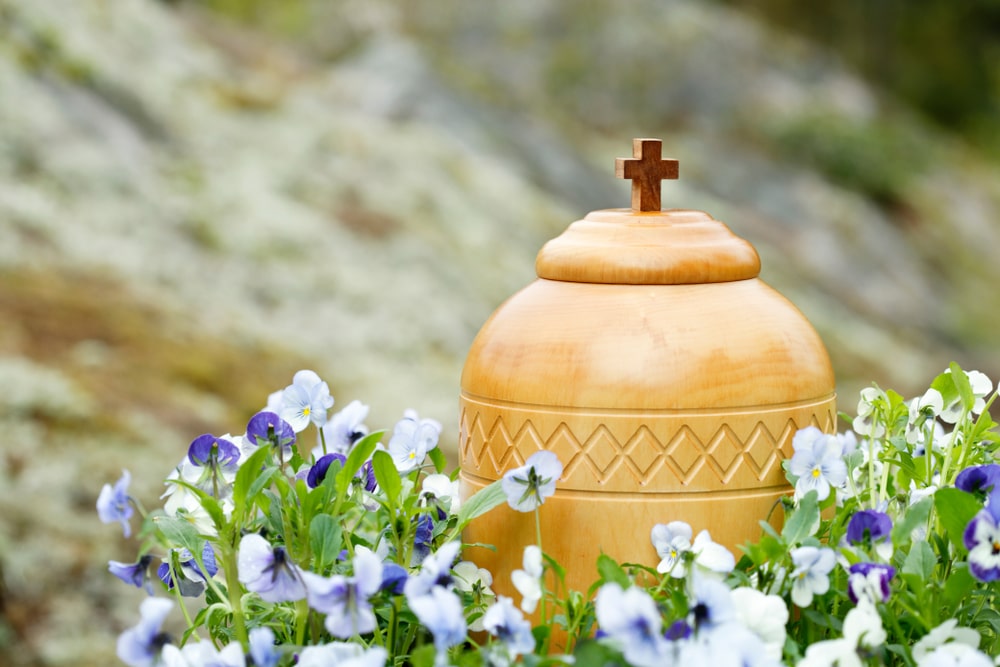 Wooden urn with cross on top, surrounded by purple flowers