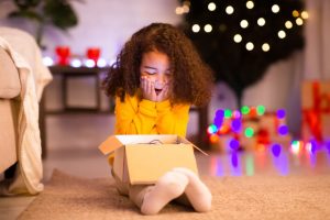 Little girl excitedly opening a gift box in front of a Christmas tree