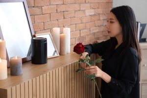 Grieving woman placing red rose next to cremation urn