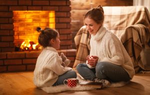 Mother and daughter sitting on floor with mugs and talking together