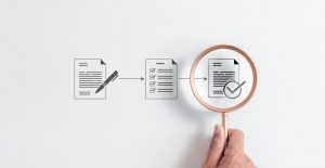 Graphic of paper and pen to paper with checklist to paper with checkmark with a magnifying glass highlighting it.