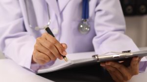Close up of doctor's hands writing on a clipboard.