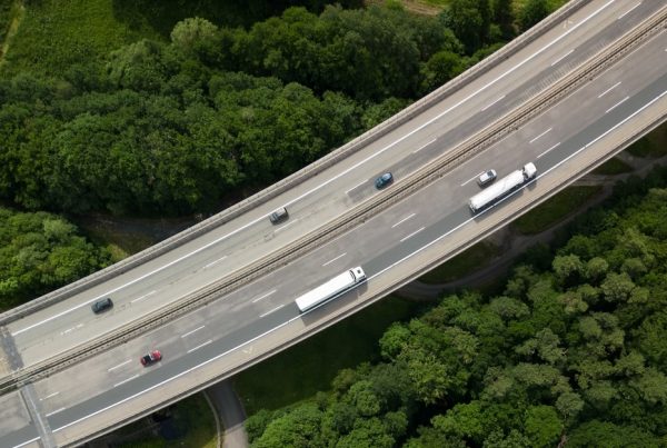 Overhead view of highway with vehicles, surrounded by trees.