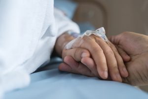 Focus on two people holding hands, one with a hospital IV inserted