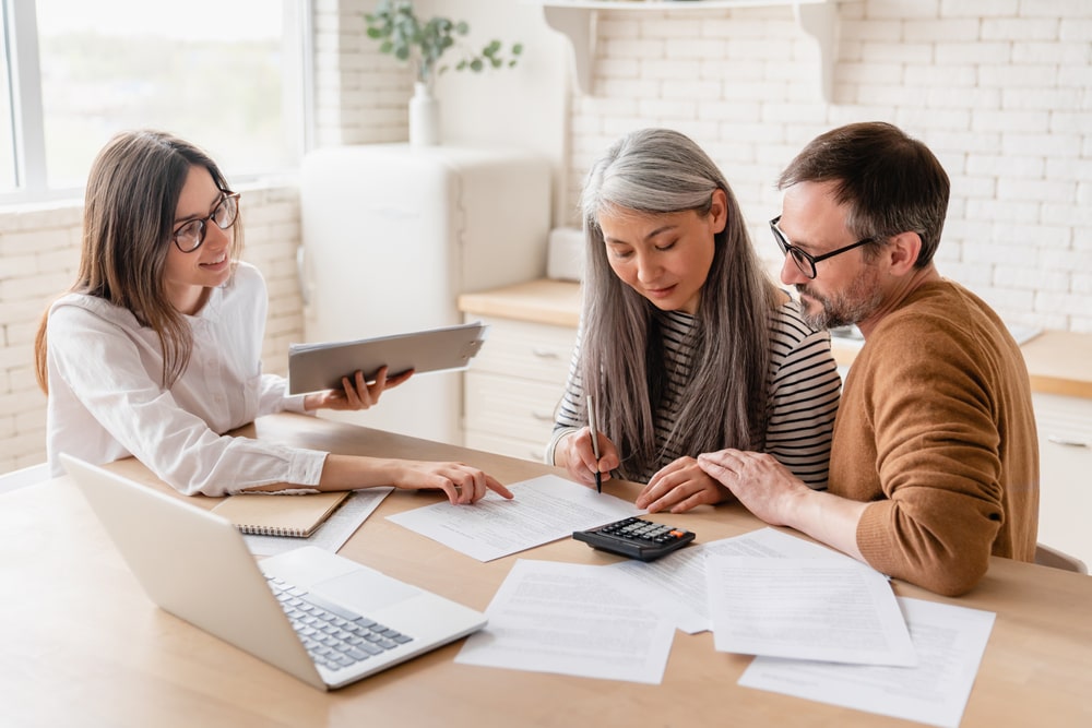Middle-aged couple sitting at table and reviewing estate planning documents with advisor