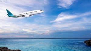 Plane in a colorful sky flying over water.