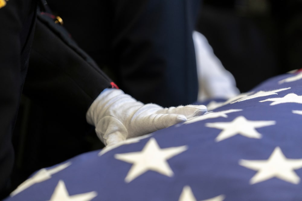 Uniformed military personnel resting hand on flag-draped casket