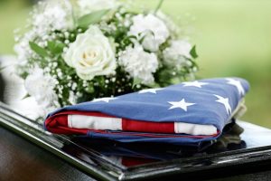 Folded American flag resting on top of a casket with white flower spray behind