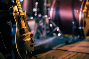 Close up of a guitar on a stand with drums in the background.