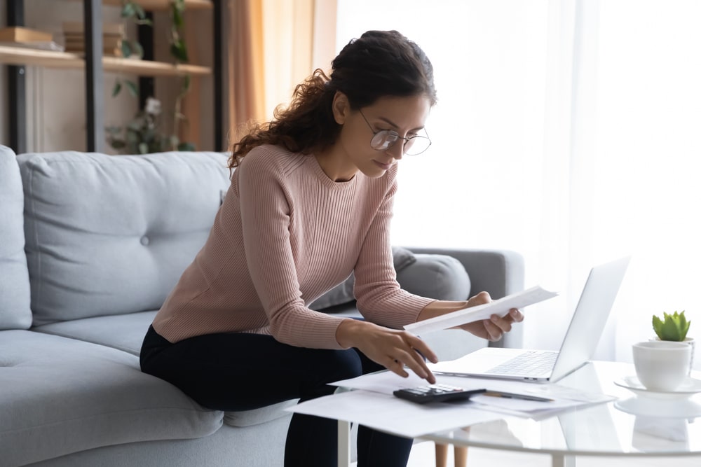 Young woman in pink sweater and glasses sitting at home and going over her estate plan