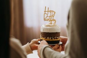 Two people holding a small chocolate birthday cake with white icing