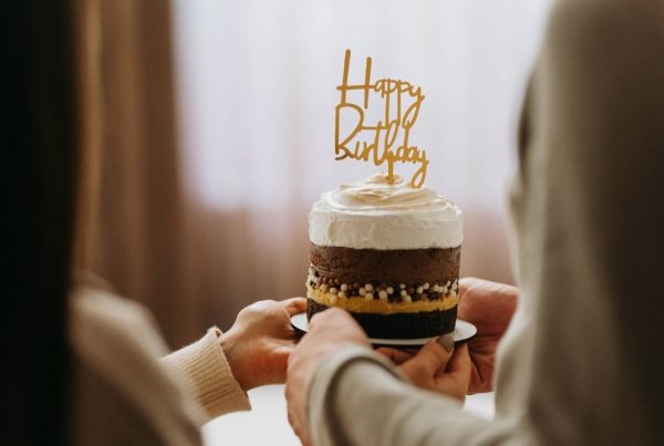Two people holding a small chocolate birthday cake with white icing