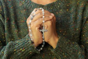 Woman in green sweater holding rosary beads