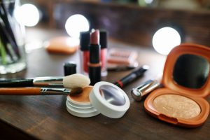 different types of makeup spread out on a table with a lighted mirror in the background