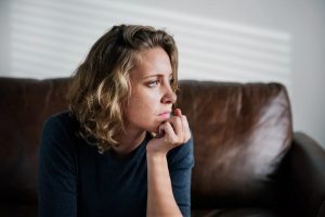 Sad woman with blue eyes sitting on couch and looking into the distance
