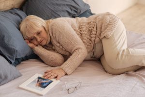Mature woman lying on bed with her hand resting on a photo of her late husband