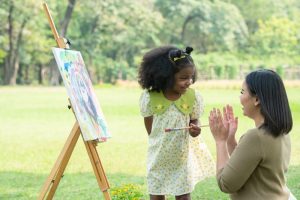 A caretaker applauding a kid while they paint outside
