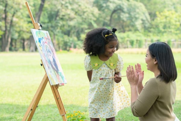 A caretaker applauding a kid while they paint outside