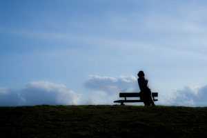 Silhouette of woman sitting on a bench with the sky behind her.