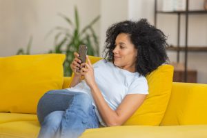 Woman sitting on yellow couch and interacting with phone and social media