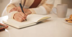 Close up of a woman's hands, writing in a journal.