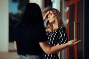 Woman with hand on her forehead, looking upset, while another woman stands beside her, frustrated.