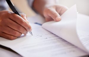 Close up of hands holding a pen and signing a document.