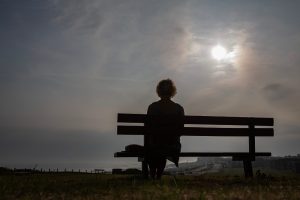 Back of woman sitting on a bench looking out at the gloomy sky.