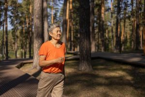 Elderly woman walking on a path with trees in the background.