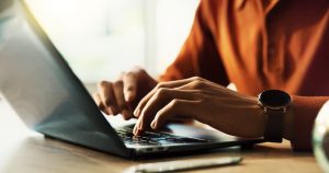 Man in orange shirt typing on laptop
