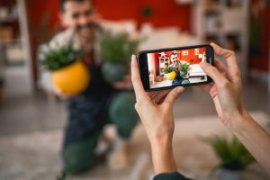 Woman taking a smartphone picture of a man holding colorful planters