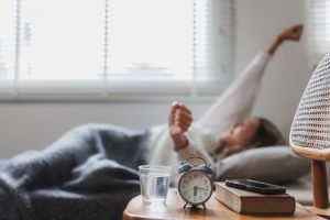 Woman laying in bed and stretching with alarm clock on the table.