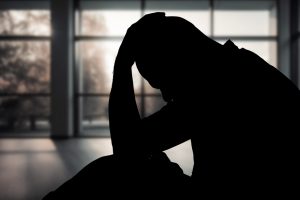 Silhouette of man sitting on the floor with hand on head.