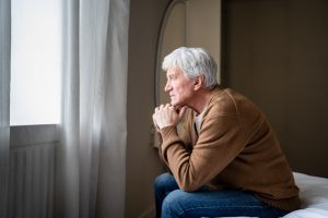 Elderly man sitting on bed and looking out the window.