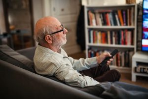 Elderly man sitting on couch and holding a remote.