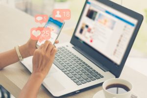 Woman sitting at table with computer and smartphone, looking at social media notifications