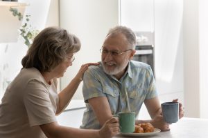 Woman with hand on man's shoulder, drinking coffee and talking