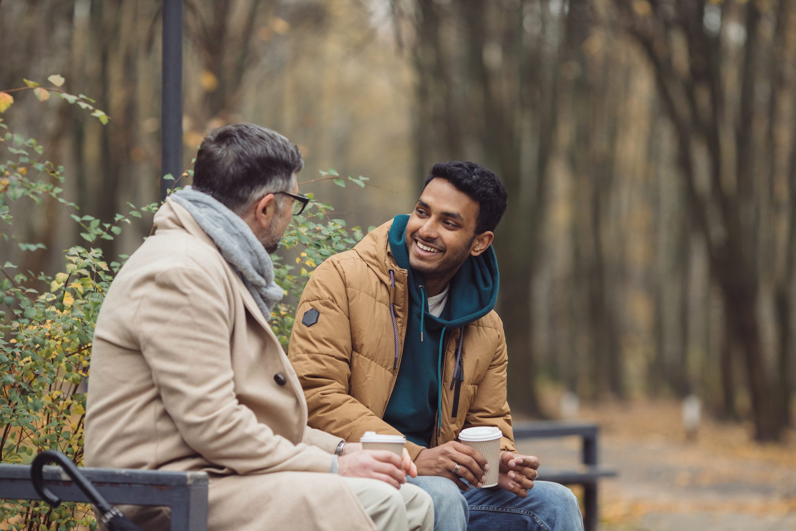 Two men drinking coffee and sitting on a bench in the park