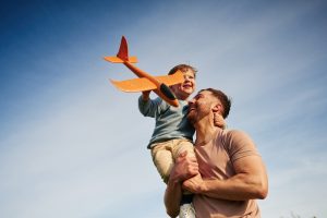 Father holding son outside as son holds a model airplane
