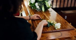 Woman placing a white rose on top of a wooden casket