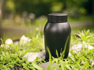 A black urn sitting outside among grass and rocks
