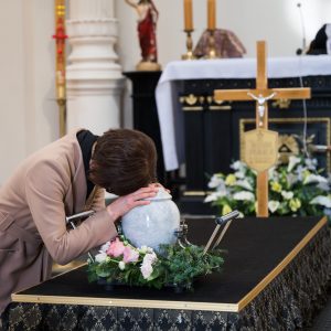 A woman placing her hands on an urn while she mourns during a Christian memorial service