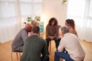 Group of people sitting in chairs in a circle listening to a woman talk.