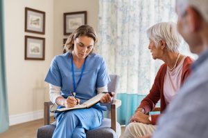 Healthcare worker writing on a clipboard while talking to elderly couple.