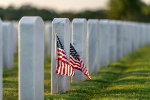 Image of a line of graves at a national cemetery with small American flags planted in ground