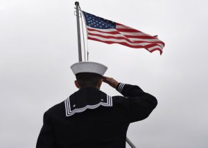 Sailor in uniform saluting the American flag on an overcast day